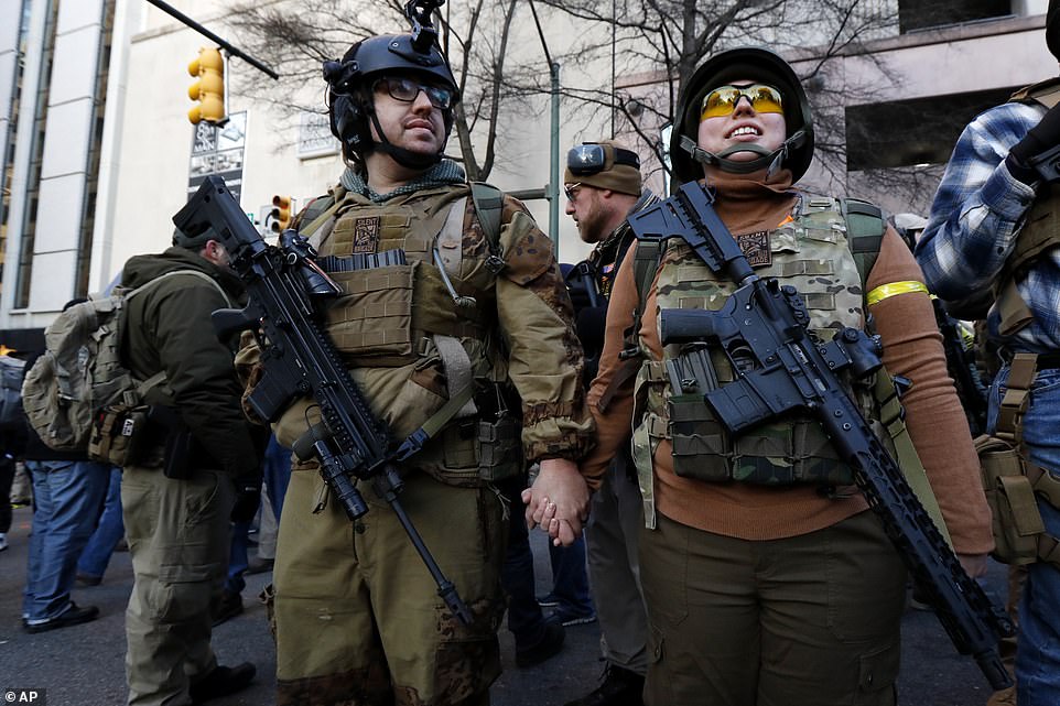 Demonstrators hold hands as they stand outside the rally proudly wearing their rifles, helmets and bullet proof vests